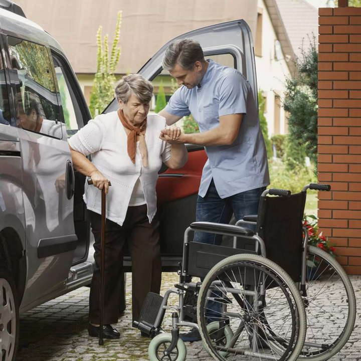 A I Love Open Arms  caregiver in a green uniform stands next to an elderly man in a workspace, both smiling, symbolizing trust and collaboration.