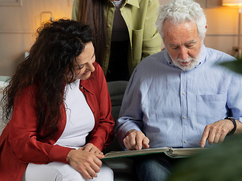 A OpenArms HCS caregiver and an elderly man sit together on a porch swing, enjoying coffee and a book, emphasizing relaxed and meaningful companionship.